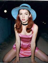 A sultry 27 year old woman with 1950s fashion wears a pink dress in an alleyway